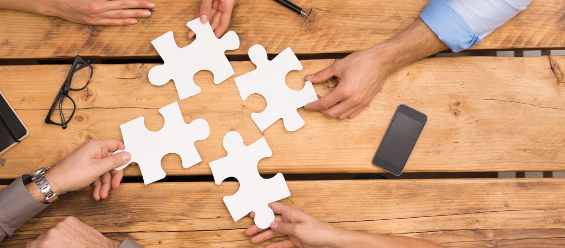 Close-up of businesspeople solving jigsaw puzzle. Closeup of business people wanting to put four pieces of puzzle together. Businesspeople trying to solve problem with the help of jigsaw puzzle.